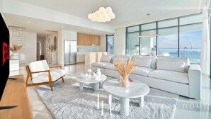 A modern living room with a white sofa, a wooden chair, and a marble coffee table. There is a large window with a view of the city and a Ferris wheel. - LUX ULTRA Luxury Palm Dubai Eye Suite (Dubai)