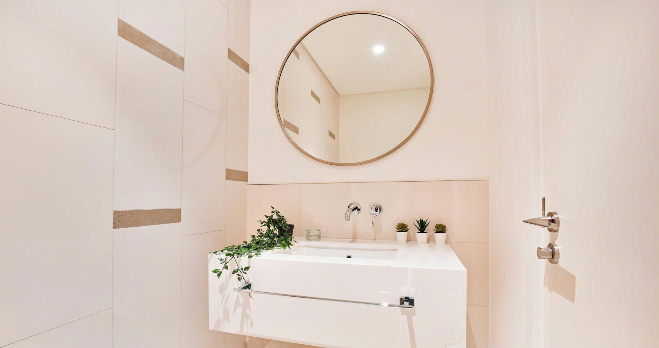 Een moderne badkamer met een wit wastafel, twee kraan en een spiegel, evenals een handdoekhouder.