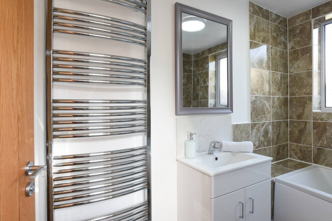 Une salle de bain au design moderne, dotée d'un porte-serviettes chromé, d'un lavabo blanc avec un miroir au-dessus, et d'un espace douche aux murs carrelés.