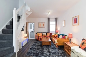 Ein modernes Wohnzimmer mit Treppe, einer Sofagarnitur, einem Couchtisch und einer Küche im Hintergrund.