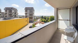 Een balkon met uitzicht op hoge gebouwen, een gele muur en een tafel met stoelen.