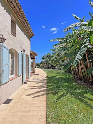 A building with a tiled roof, a covered walkway, and a grassy area with banana trees. - Stunning Villa with Pool, BBQ and Fitness - 4 Suite Bedrooms - 8 Guests (Tourrettes-sur-Loup)