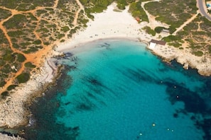 An aerial view of a coastal area with a beach, rocky shoreline, and a few buildings.