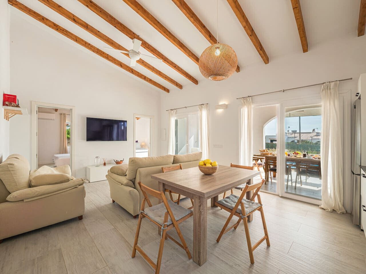 A spacious living room with a wooden dining table, sofas, and a TV.