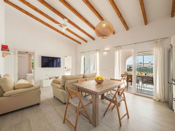 A spacious living room with a wooden dining table, sofas, and a TV.