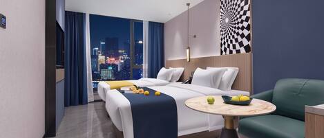 A modern hotel room with a large bed, a green sofa, a small round table, and a view of the city at night.