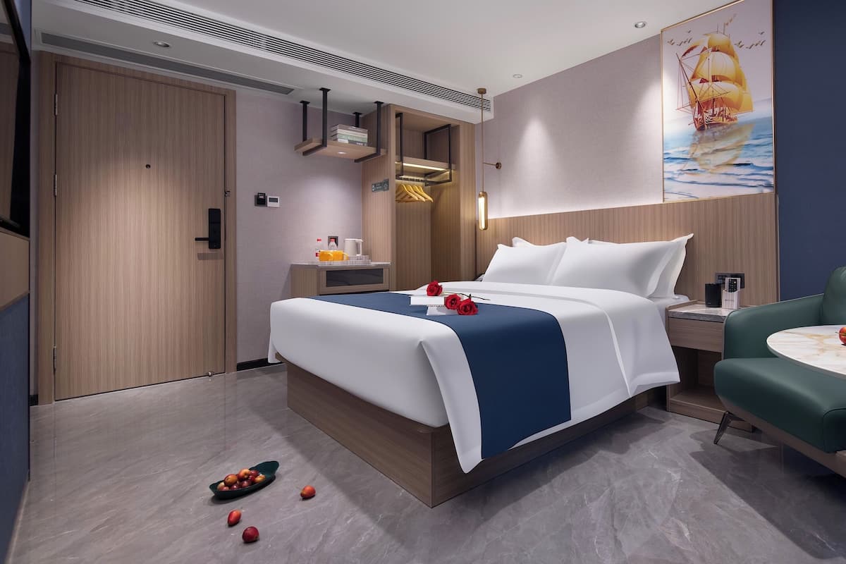 Quarto de hotel moderno com uma cama grande, mesa de cabeceira, uma cadeira e uma obra de arte na parede.