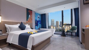 A modern hotel room with a large bed, a sitting area, and a view of the city skyline. - Hiatu Hotel   Huidong Huangbu Branch (Huizhou)