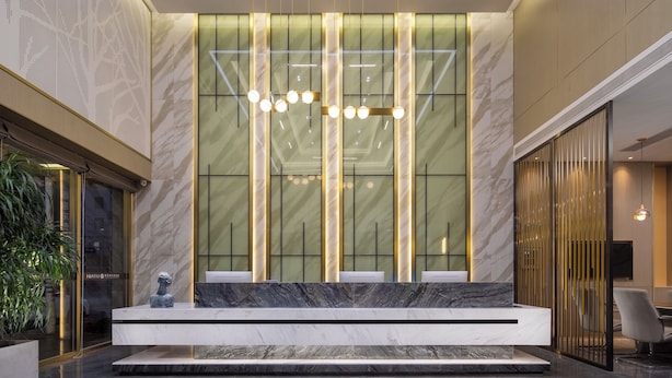 A reception area with a marble counter, modern lighting, and a large glass wall with vertical lines. - Hiatu Hotel   Huidong Huangbu Branch (Huizhou)
