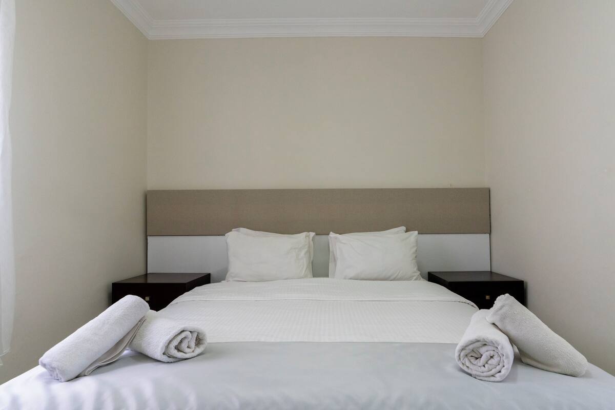 A hotel room with a bed, two nightstands, and rolled towels.