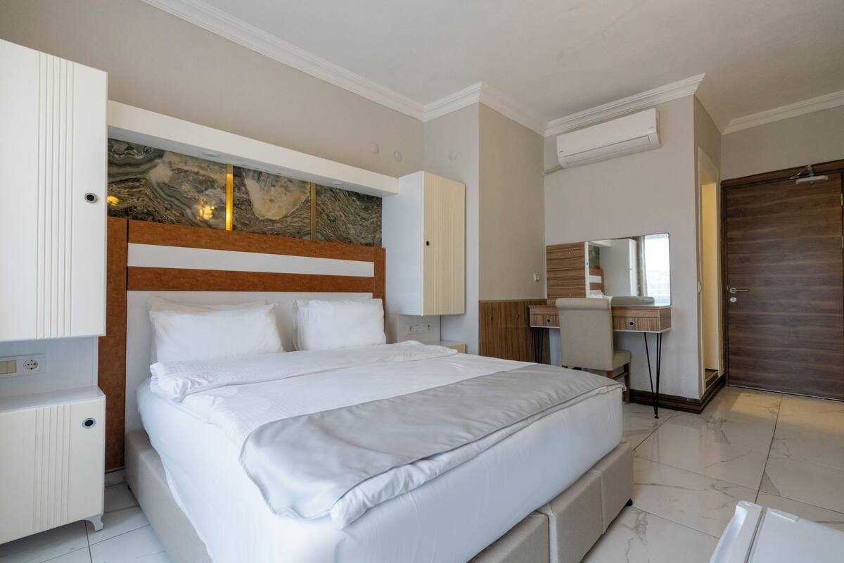 A hotel room with a large bed, a wooden headboard, a marble accent wall, a desk with a mirror, and a wardrobe.