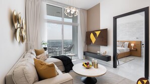 A modern hotel room with a large window, a sofa, a round coffee table with fruit, a TV, and a balcony with a view. - Vogue | Skyz by Danube near Dubai Miracle Garden (Dubai)