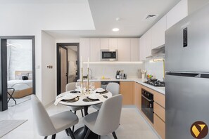 A modern kitchen with a dining area, a microwave, a stove, and a dishwasher. - Vogue | Skyz by Danube near Dubai Miracle Garden (Dubai)