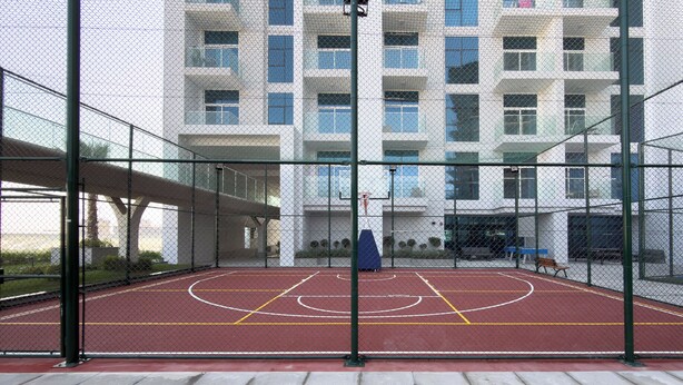An outdoor basketball court enclosed by a chain-link fence, with a building in the background. - Vogue | Skyz by Danube near Dubai Miracle Garden (Dubai)