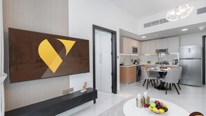 Eine moderne Küche mit Essbereich, einem an der Wand befestigten Flachbildfernseher und einer Obstschale auf einem weißen Tisch.