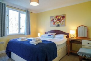 Habitación de hotel con cama, dos lámparas de noche, un escritorio con silla, un espejo y un cuadro en la pared.