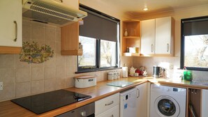 A compact kitchen with a built-in oven, a washing machine, and a window providing natural light. - Swift Cottage, Norfolk Broads riverside holiday rental with boat mooring (Potter Heigham)