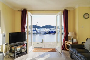 Habitación con televisor, sofá, lámpara y vistas a barcos en un puerto deportivo.
