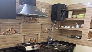 Cocina compacta con estufa a gas, un lavamanos y una campana extractora negra. Se observan estantes con utensilios de cocina y objetos decorativos.