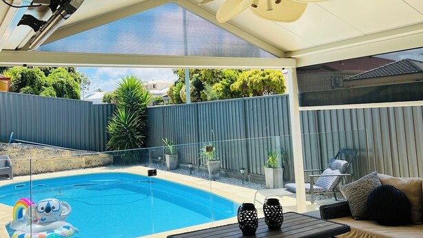 Et overdækket udendørs område med swimmingpool, ventilator og udendørs møbler.