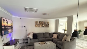 En moderne stue med en grå hjørnesofa, et sofabord, et fladskærms-TV og et billede på væggen.