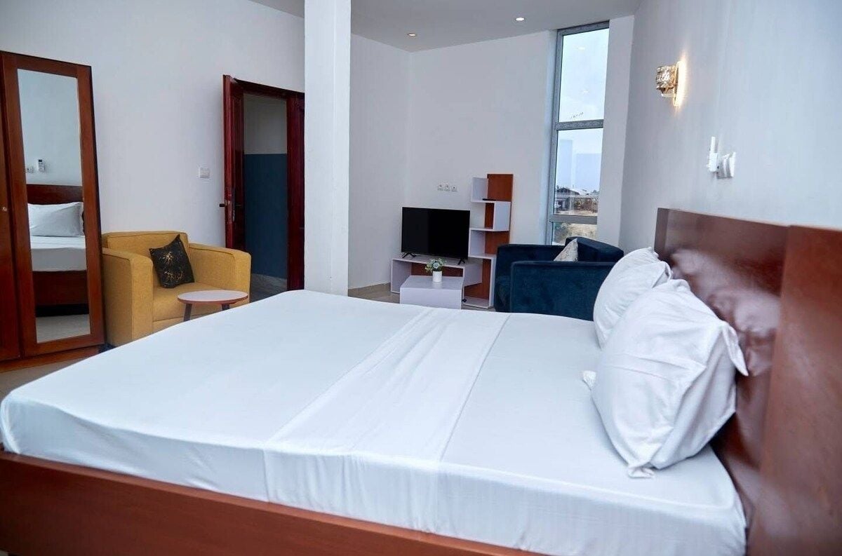 Quarto de hotel com uma cama grande, televisão, sofá e vista da cidade.