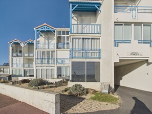 Un immeuble à plusieurs étages doté de balcons, une enseigne indiquant « Résidence FORCE 5 », et un jardinier en béton planté d’arbustes.