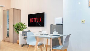A modern office space with a desk, two chairs, a television displaying 'NETFLIX', a microwave, and a potted plant. - LUX The Marina View Suite 2 (Dubai)