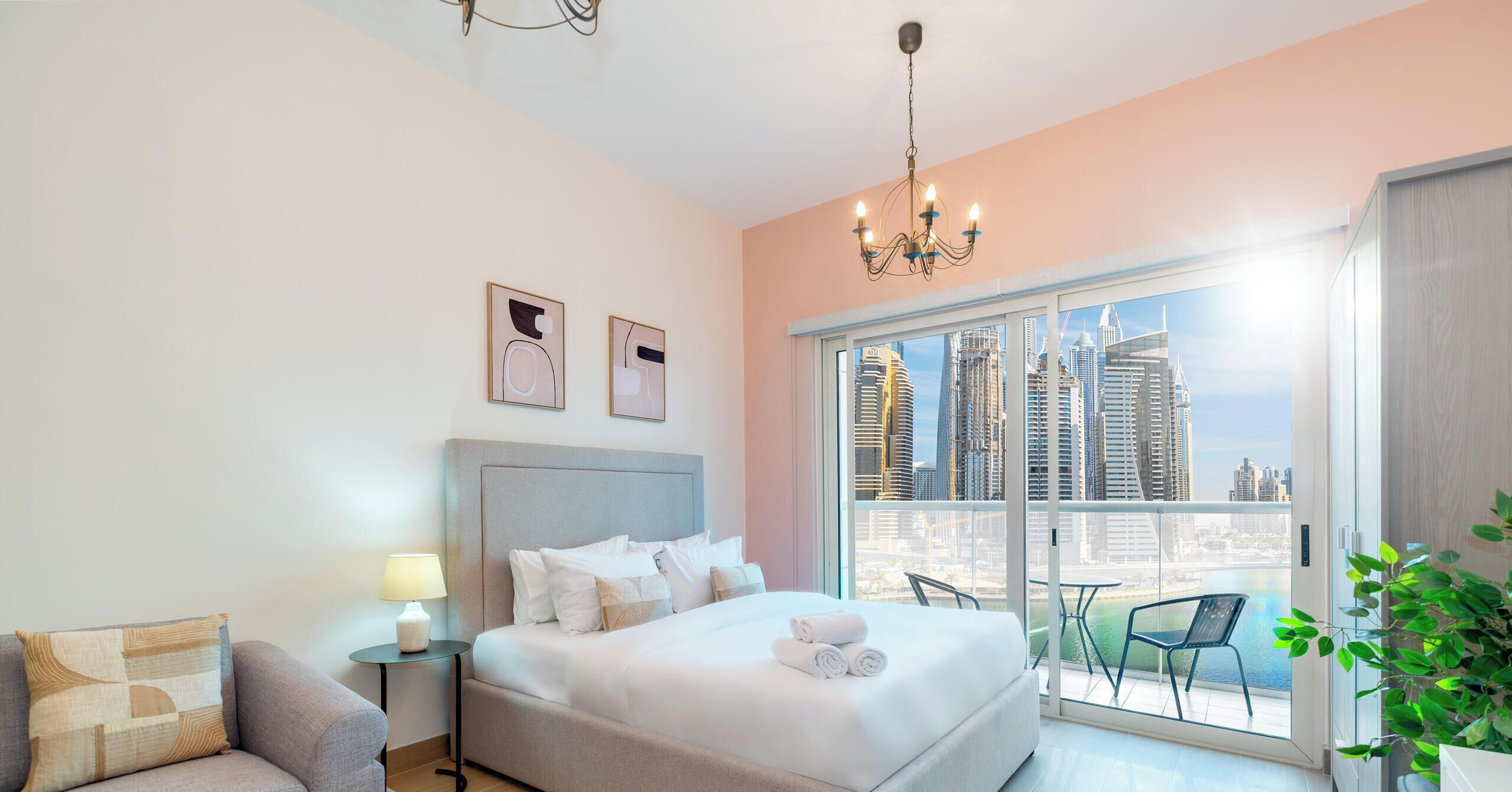 A modern hotel room with a large bed, a nightstand, a lamp, and a view of a cityscape through a balcony.