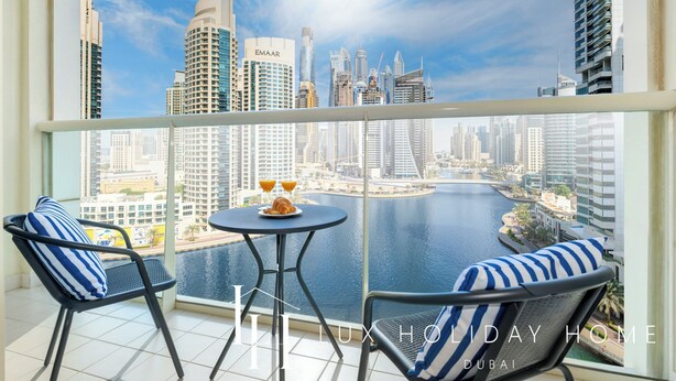 A balcony with two chairs and a small table, overlooking a cityscape and water. - LUX The Marina View Suite 2 (Dubai)