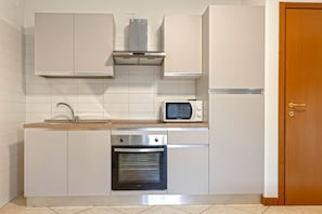 A compact kitchen with white cabinetry, a built-in oven, a microwave, and a stainless steel range hood.