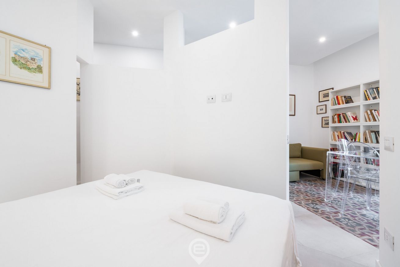 Un dormitorio moderno con cama, sofá, estantería y una silla transparente.