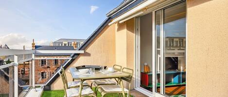 A balcony with a table and chairs, a small artificial grass area, and a view of a building in the background.