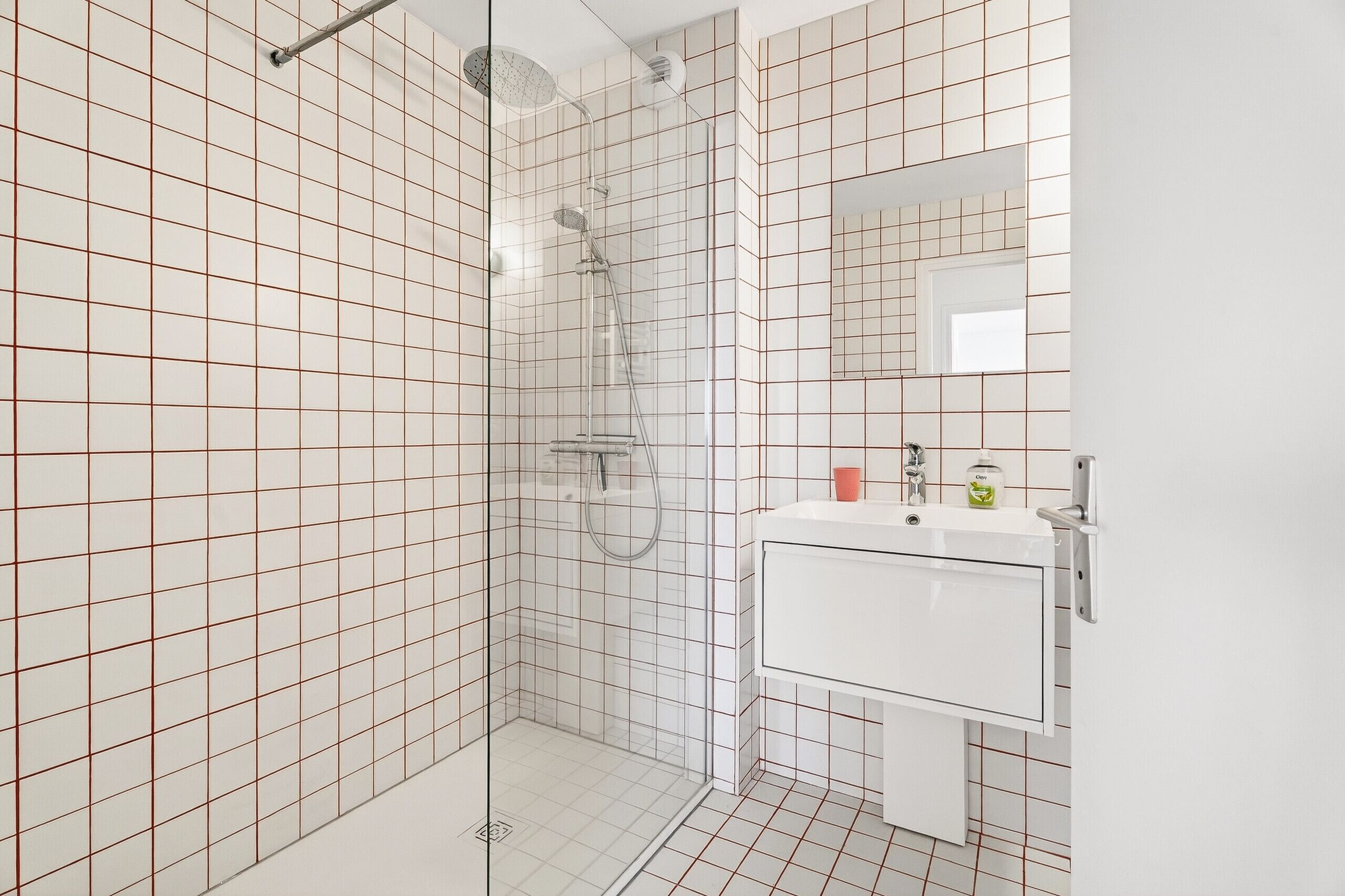 A modern bathroom with a glass-enclosed shower, white tiled walls, and a white vanity with a mirror.