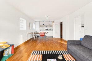 Ein modernes Wohnzimmer mit einem grauen Sofa, einem Streifenmuster-Teppich und einem Essbereich mit Tisch und Stühlen.