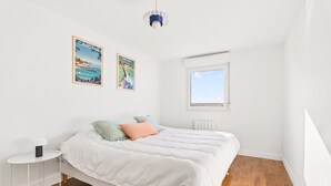 A bedroom with a bed, a small white side table, a window, and two posters on the wall. - Apartment for 2, terrace, near the beach (Dinard)