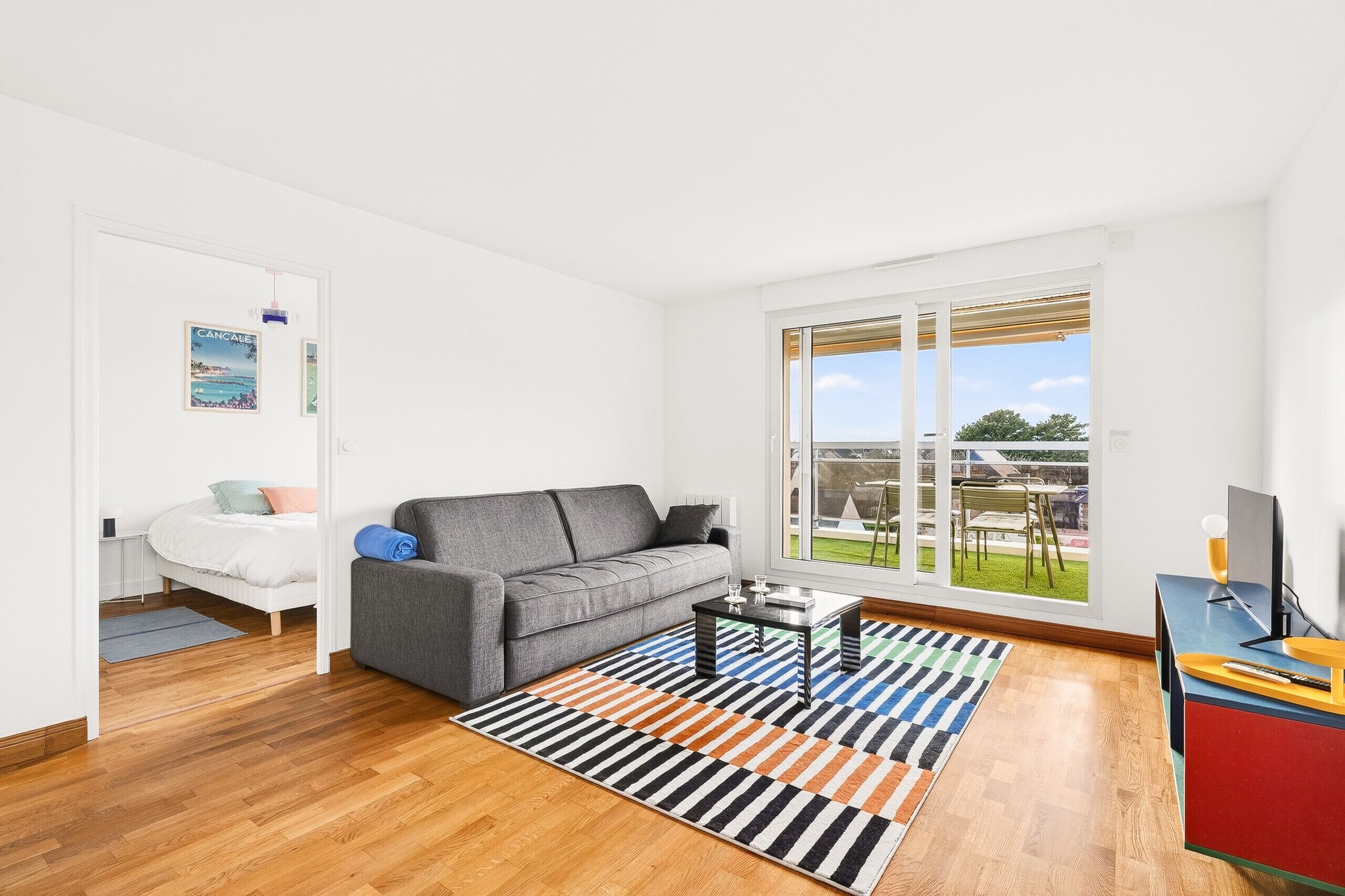 A modern living room with a grey sofa, a coffee table, and a large window offering a view of the outdoors.