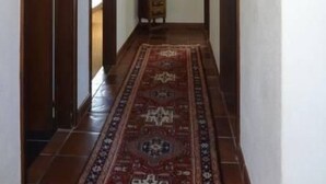 Un pasillo estrecho con puertas de madera, un tapete estampado y una lámpara fijada a la pared.