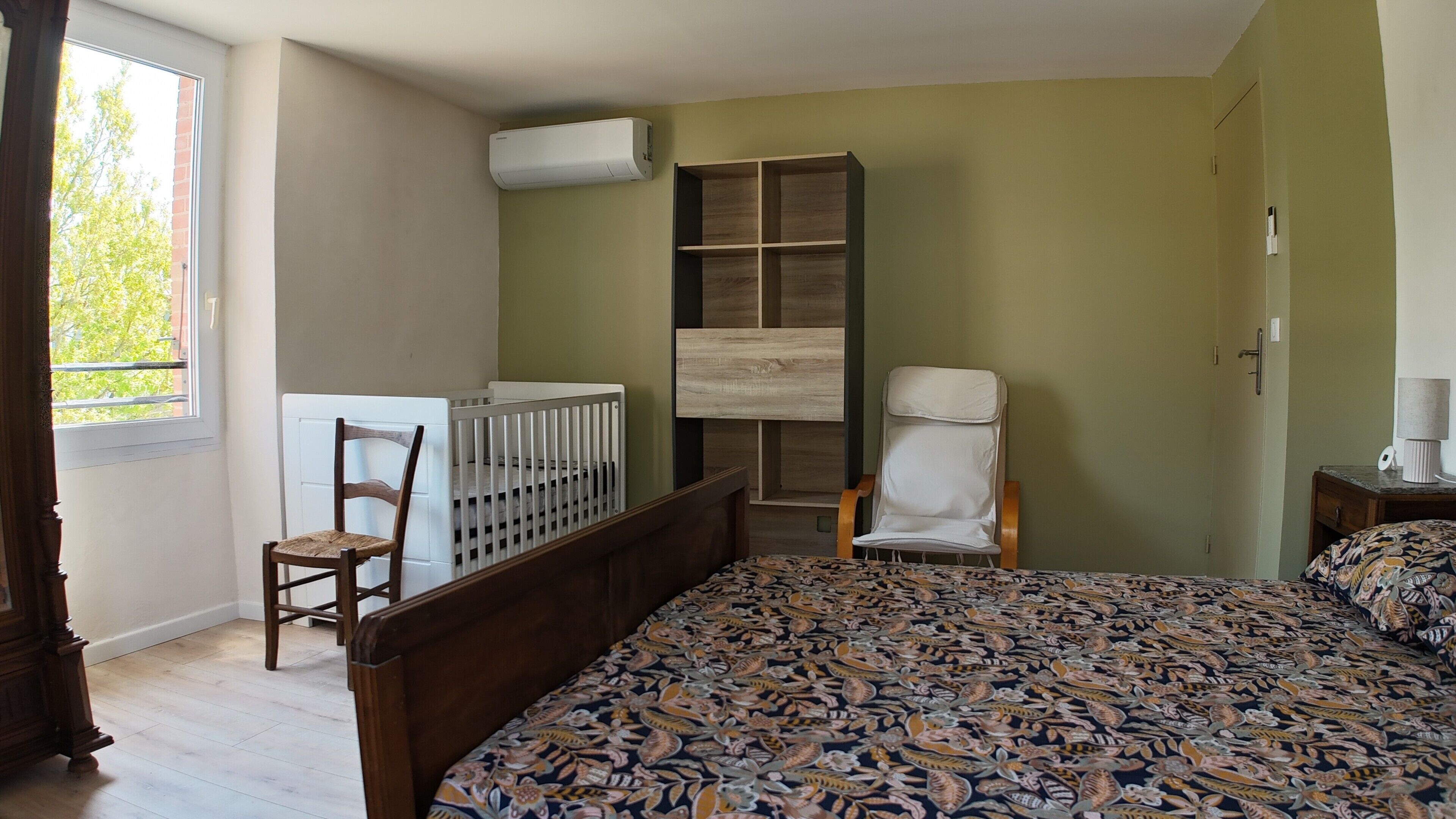 Ein Schlafzimmer mit Bett, Babybett, Stuhl, Kleiderschrank und Klimaanlage.