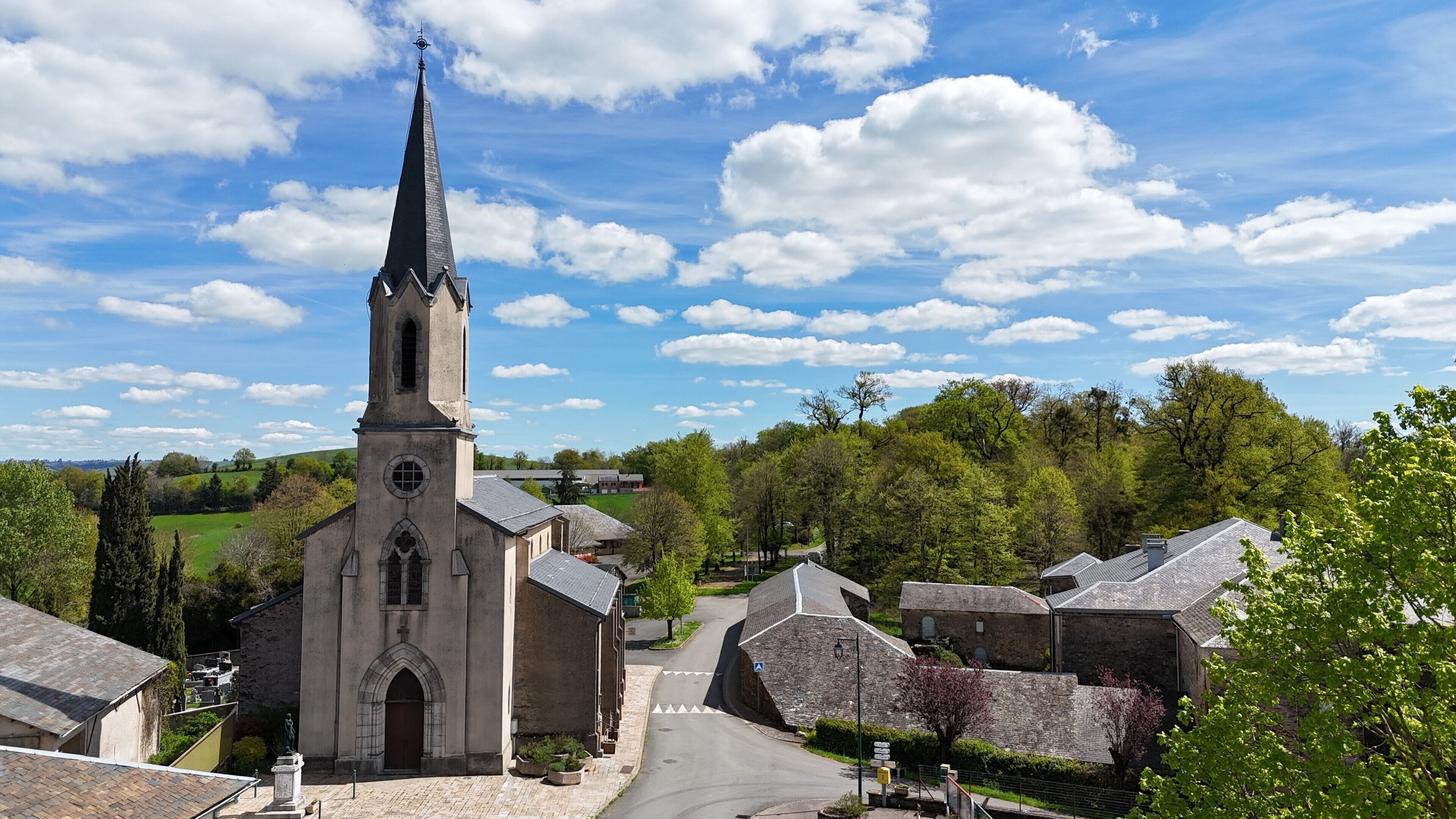 A church with a tall steeple, surrounded by stone buildings and greenery.