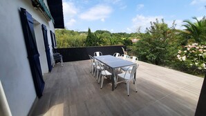 Eine Terrasse mit Tisch und Stühlen, umgeben von einer schwarzen Mauer und viel Grün.