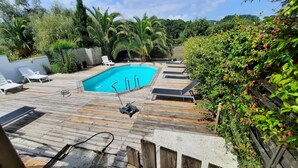 Ein Schwimmbecken mit Holzterrasse, Liegestühlen und einem Garten mit verschiedenen Pflanzen.