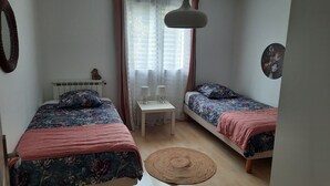 Ein kleines, helles Schlafzimmer mit zwei Einzelbetten, einem kleinen Tisch und einer Hängelampe.