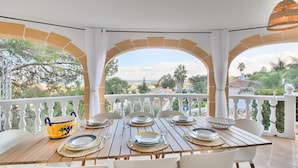 Eine Terrasse mit Esstisch, weißen Stühlen und einer dekorativen Schale.