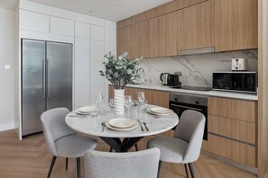 A modern kitchen with a built-in microwave, a stainless steel refrigerator, and a dining area with a round table set for four. - Beachfront Living with Marina Skyline Views (Dubai)