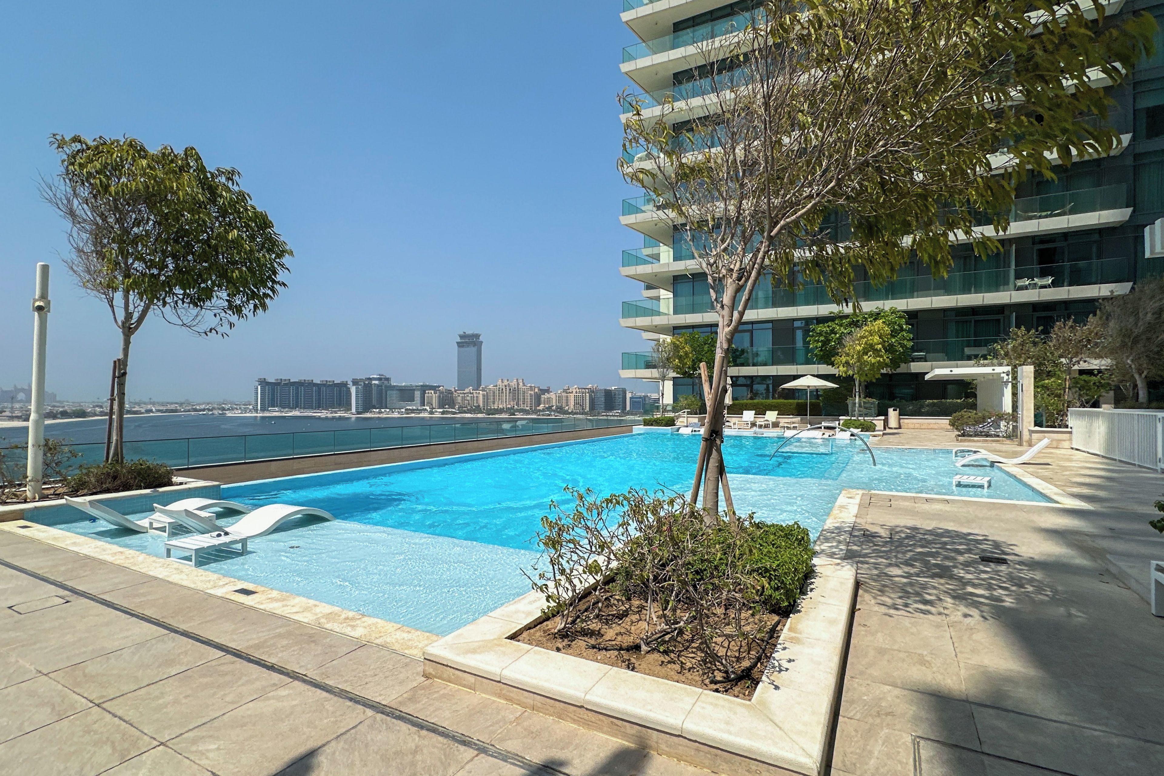 A rooftop swimming pool with a view of the city skyline and a body of water in the background.