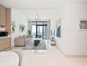 Ein modernes Wohnzimmer mit Sofa, Couchtisch und Fernseher. Ein großes Fenster bietet Blick auf Gebäude.