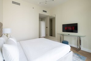A hotel room with a bed, a glass table with a television displaying 'NETFLIX', and a door leading to another room. - Beachfront Living with Marina Skyline Views (Dubai)