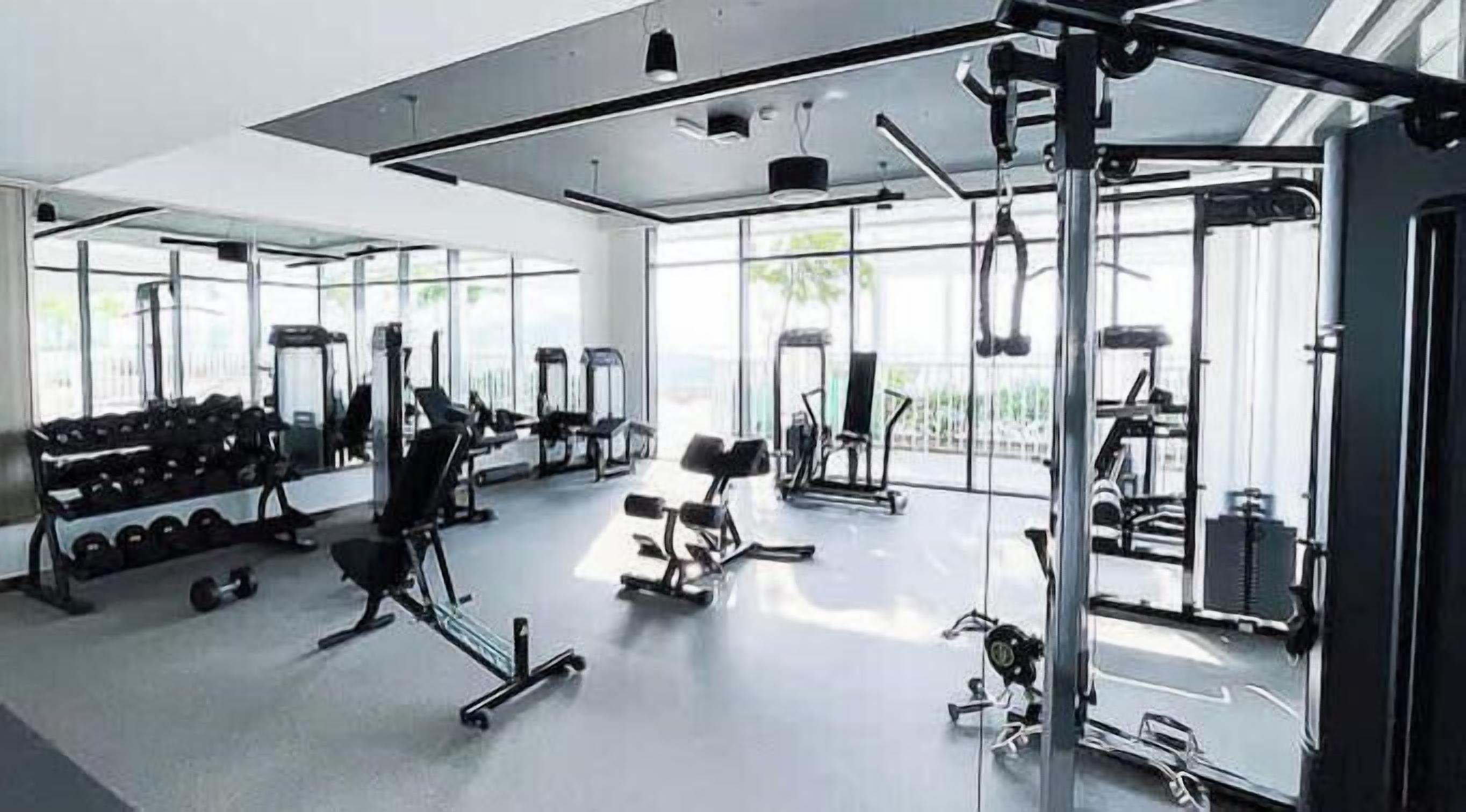 A modern gym with various exercise equipment, large windows, and a clean, spacious layout.