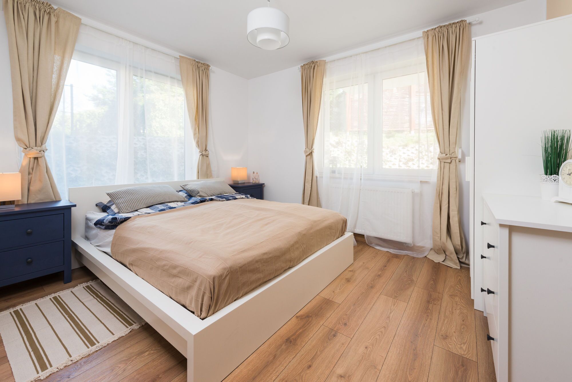 Un dormitorio con cama, mesitas de noche, lámpara, radiador y cortinas.